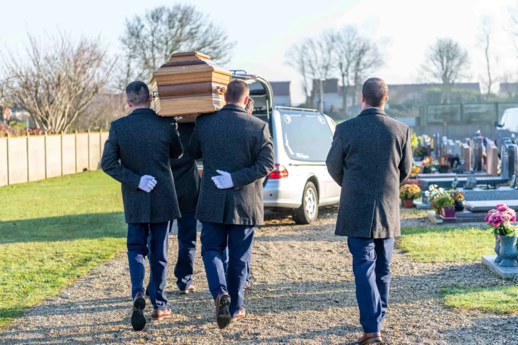 Quatre porteurs portant un cercueil en bois sur leurs épaules lors d'une cérémonie.
