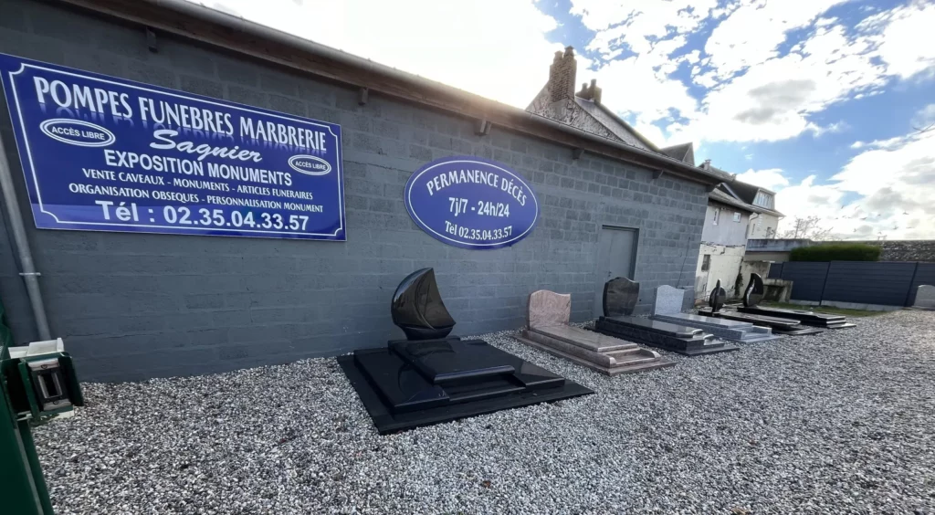 Parc d'exposition de monuments funéraires et caveaux devant l'enseigne des Pompes Funèbres Marbrerie Sagnier.