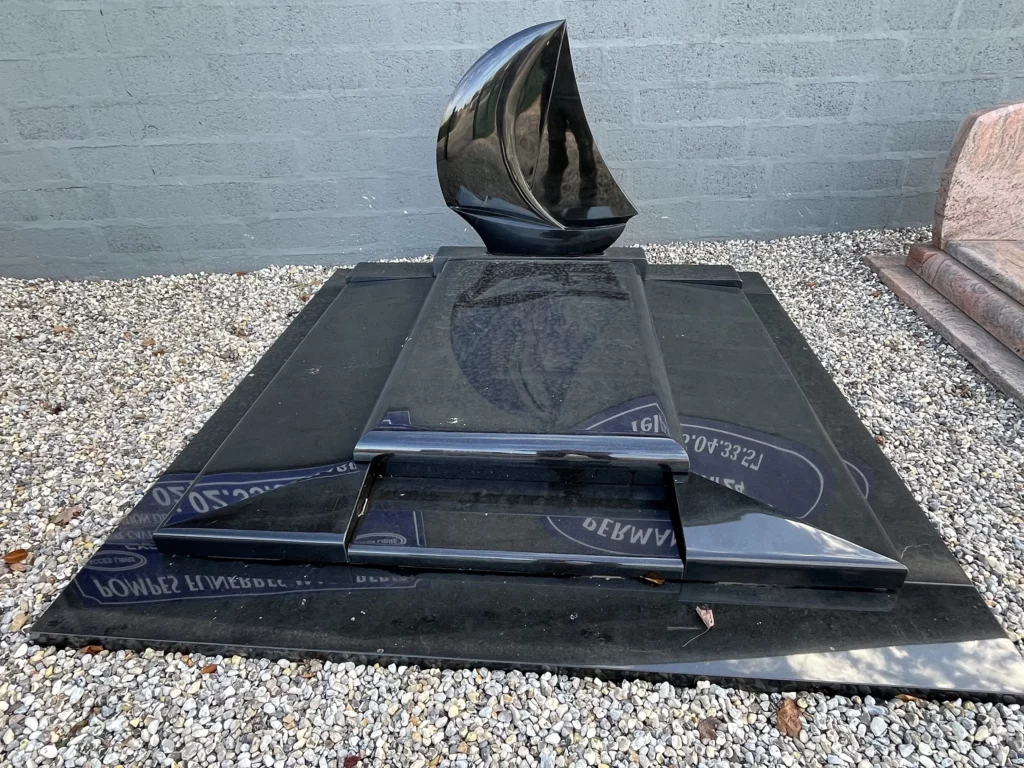 Monument funéraire design en granit noir poli surmonté d'une stèle sculptée en forme de voile de bateau.
