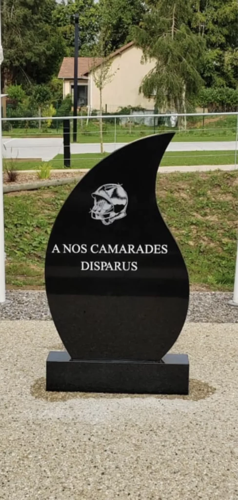 Stèle funéraire commémorative en granit noir en forme de flamme dédiée aux camarades disparus.