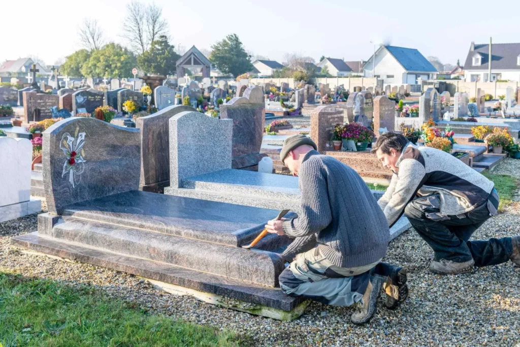 Deux marbriers funéraires travaillant à l'installation d'une tombe en granit.