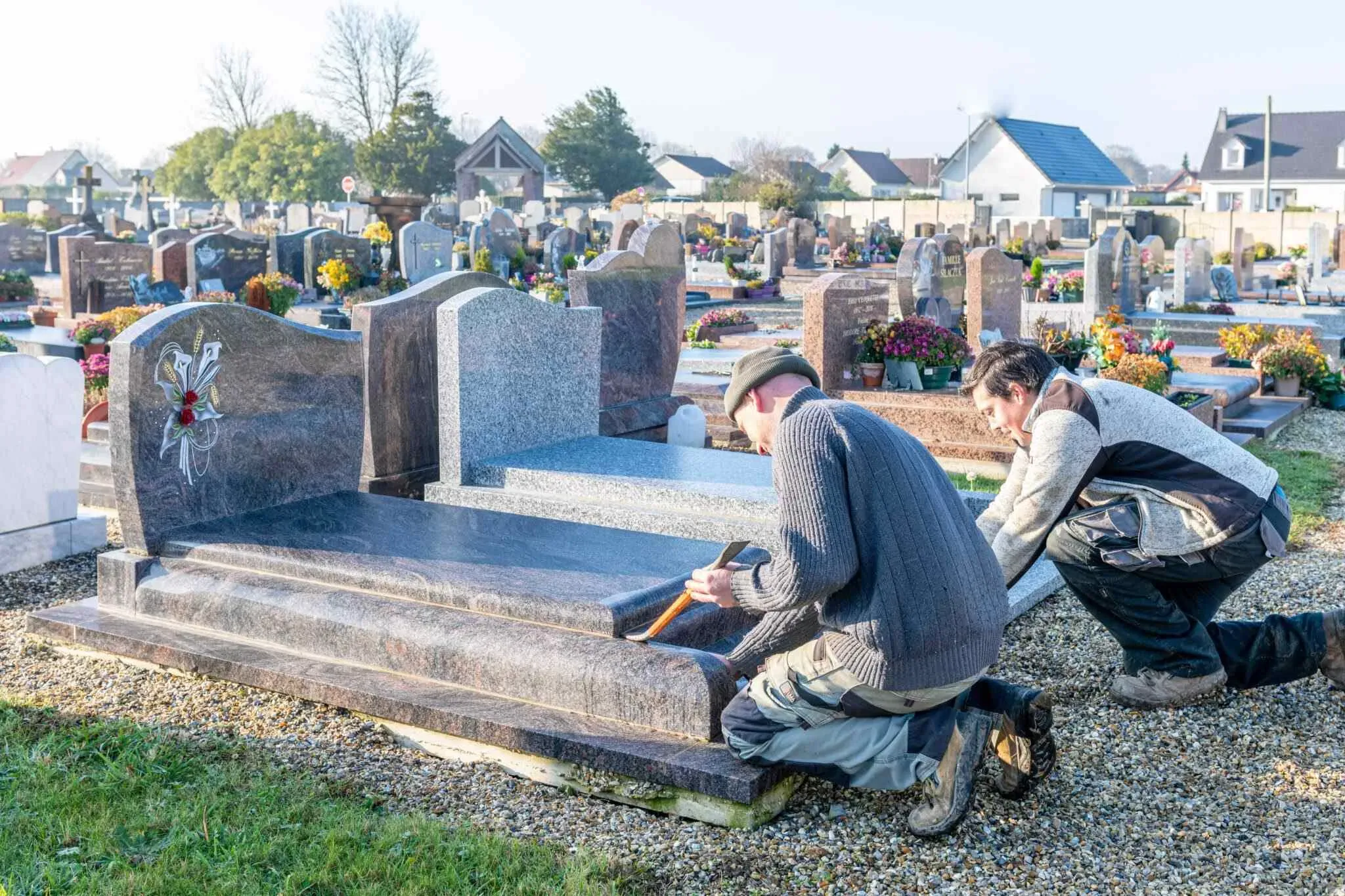 Deux marbriers funéraires travaillant à l'installation d'une tombe en granit.