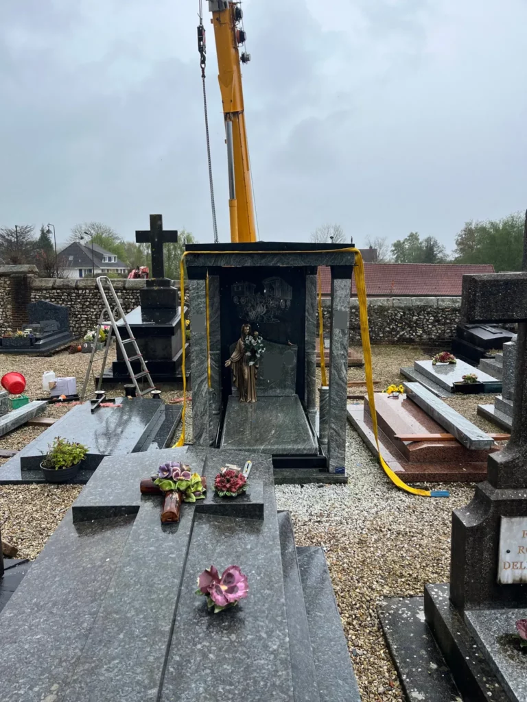 Installation d’une chapelle funéraire en granit à l’aide d’une grue de levage dans un cimetière.